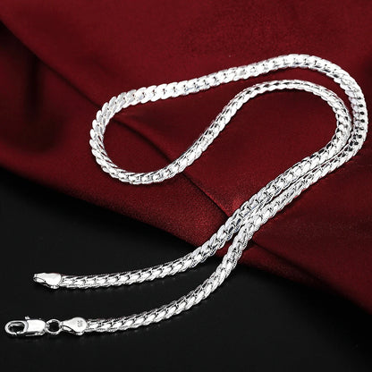 Silver chain necklace on a dark surface with a red fabric background